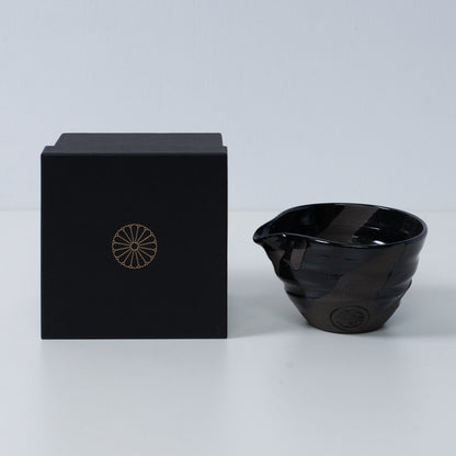 Japanese matcha bowl with spout "Sumi Black" pottery next to a black gift box with a gold imperial chrysanthemum crest, Kyoto ceramics.