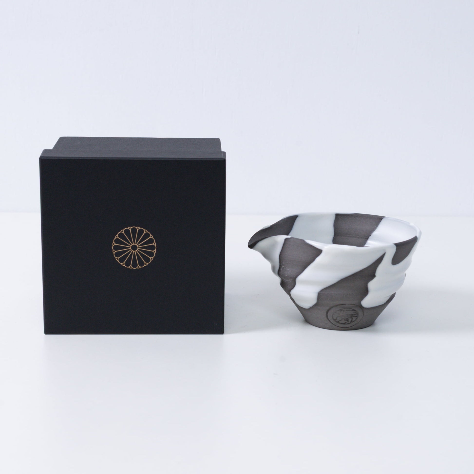 Japanse matcha kom met tuit "White Flow" aardewerk naast een zwarte geschenkdoos met een gouden chrysant-embleem, gemaakt in Japan.