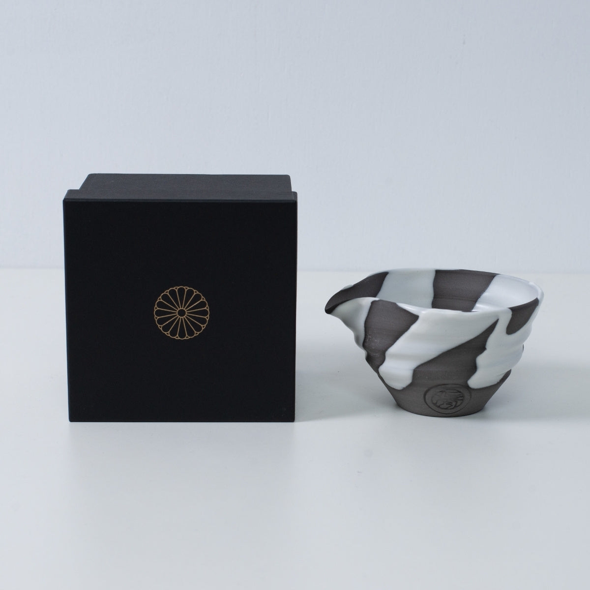Japanische Matcha-Schale mit Ausguss „White Flow“ aus Keramik, daneben eine schwarze Geschenkbox mit goldenem Chrysanthemen-Wappen, hergestellt in Japan.