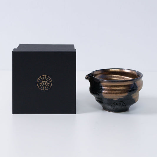 Gold and black Japanese matcha bowl with spout "Zen" pottery next to a black gift box with a gold chrysanthemum crest, made in Japan.