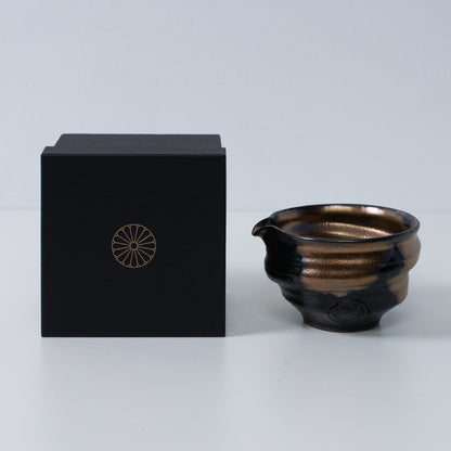 Gold and black Japanese matcha bowl with spout "Zen" pottery next to a black gift box with a gold chrysanthemum crest, made in Japan.