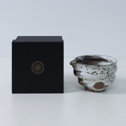 Brown and white Japanese matcha bowl with spout "Zui" pottery next to a black gift box with a gold imperial chrysanthemum crest, from Japan.