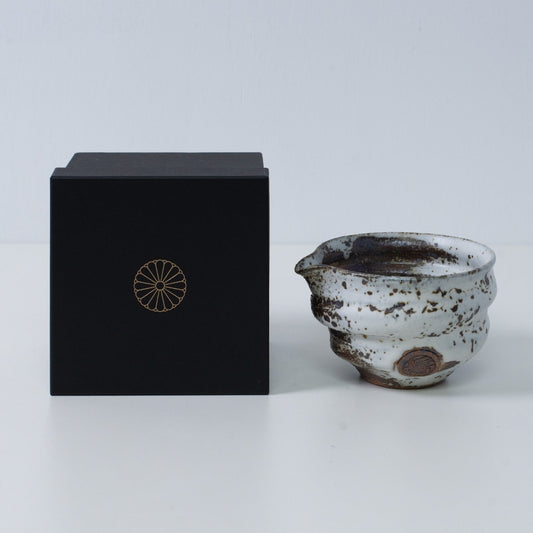 Brown and white Japanese matcha bowl with spout "Zui" pottery next to a black gift box with a gold imperial chrysanthemum crest, from Japan.