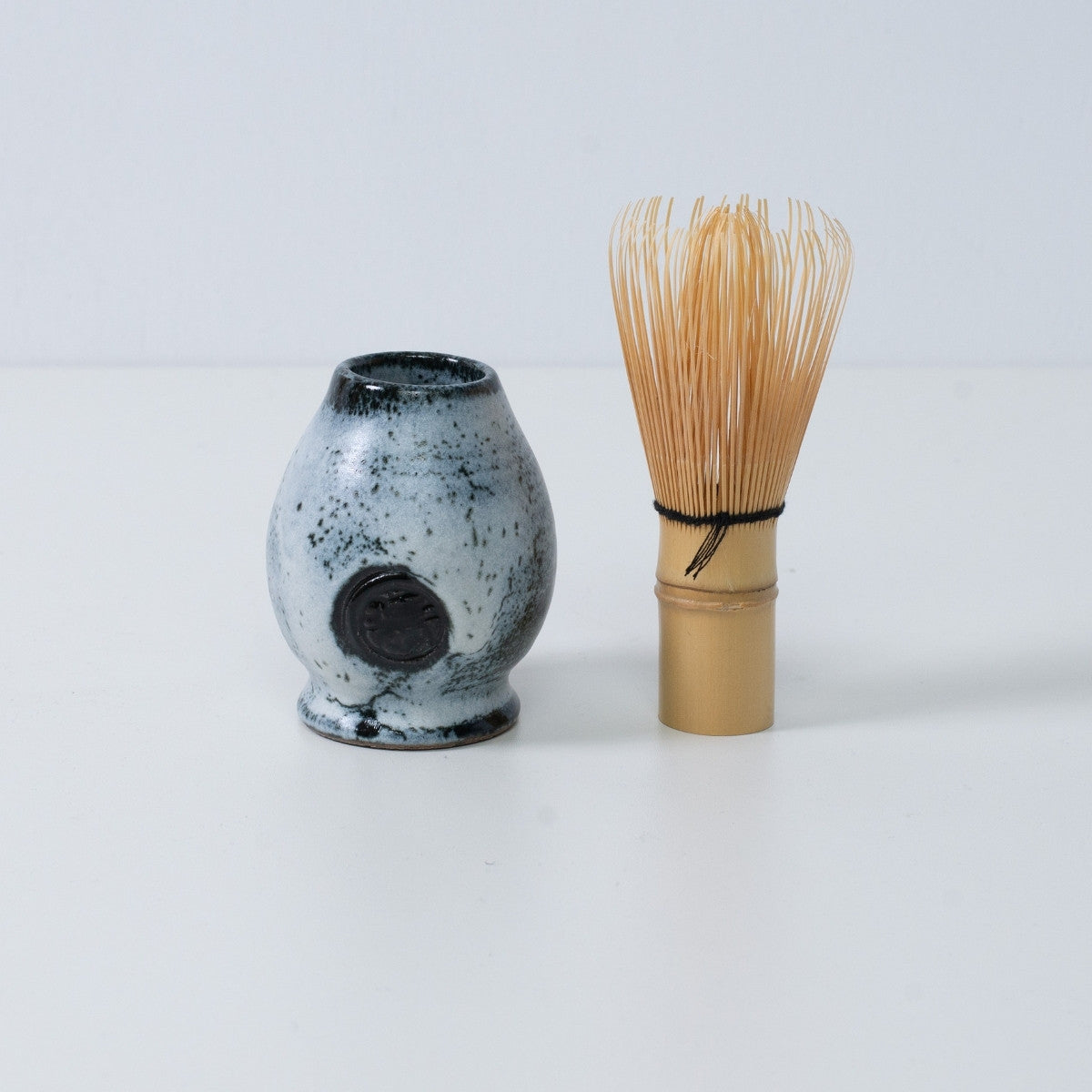 White and black Japanese matcha whisk stand "Creative Cloud" pottery standing next to a traditional bamboo matcha tea whisk, Japan.