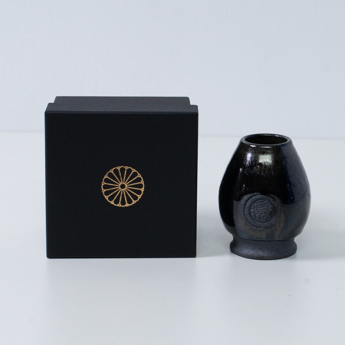 Deep blue Japanese matcha whisk stand "Dignity Blue" pottery next to a black gift box with a gold chrysanthemum crest, from Japan.