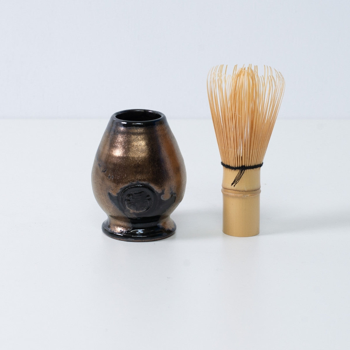 Gold and black Japanese matcha whisk stand "Zen" pottery standing next to a traditional bamboo matcha tea whisk chasen, Japan.