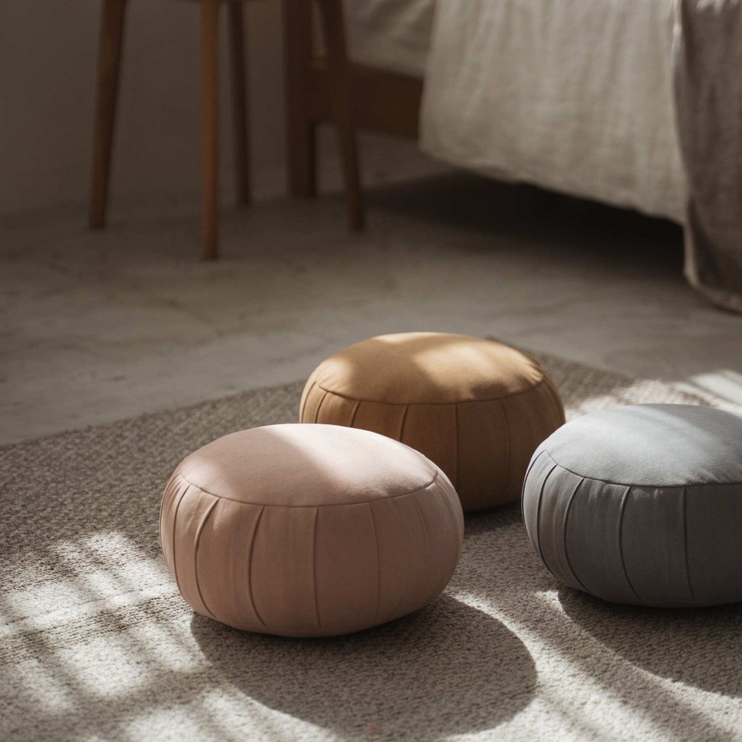 Set of three japanese zafu meditation cushions placed on a floor rug in a calm bedroom setting with sunlight.