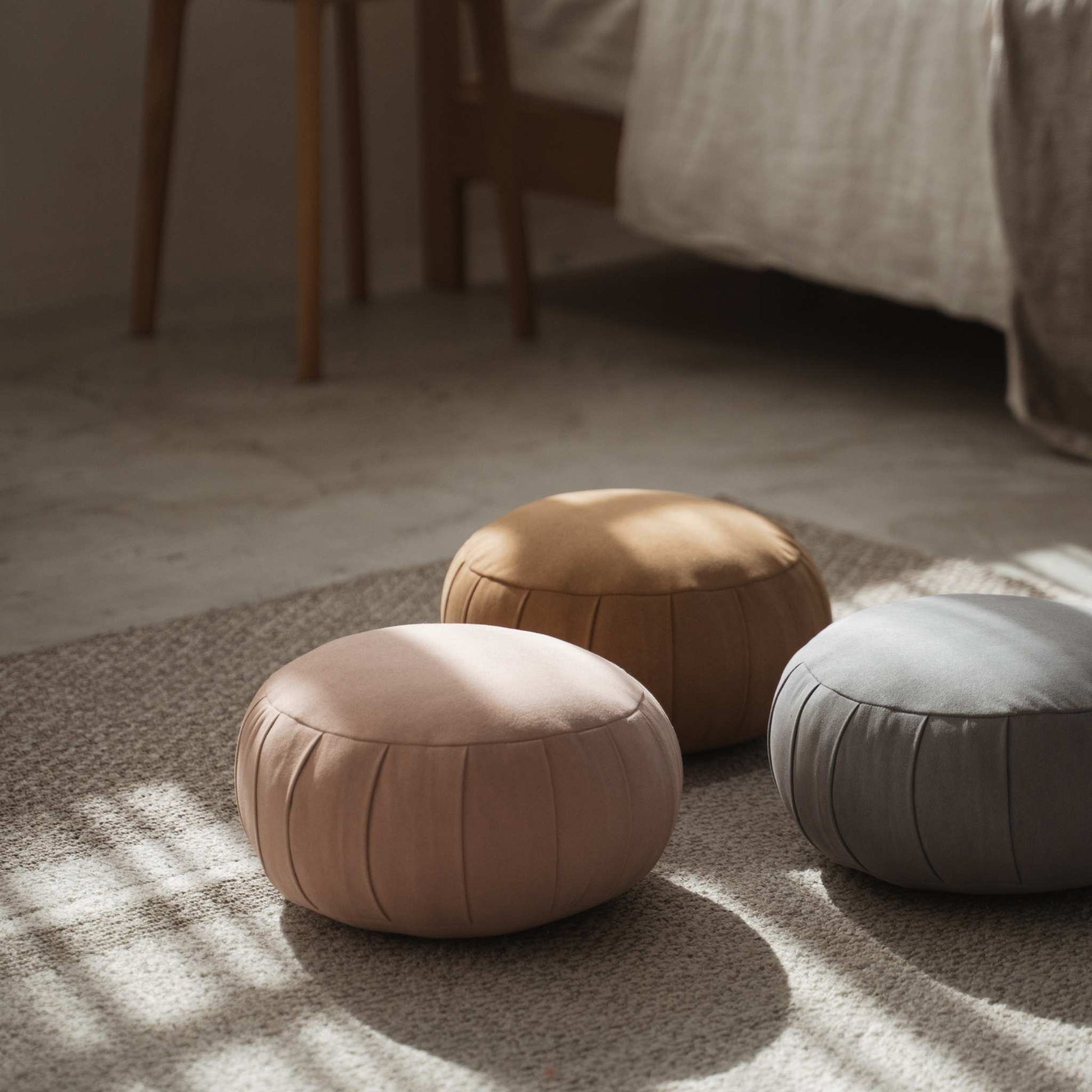 Set of three japanese zafu meditation cushions placed on a floor rug in a calm bedroom setting with sunlight.