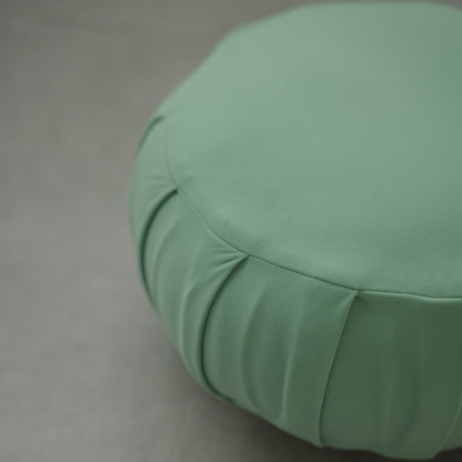 Close-up of a mint green Japanese meditation cushion (zafu), showing its detailed pleats and smooth fabric on a modern grey floor for yoga.