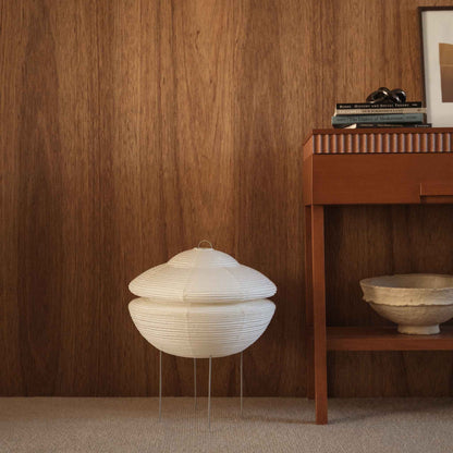 Unlit Japanese paper floor lamp Gemini 01 standing on a carpeted floor next to a wooden console table against a wooden wall
