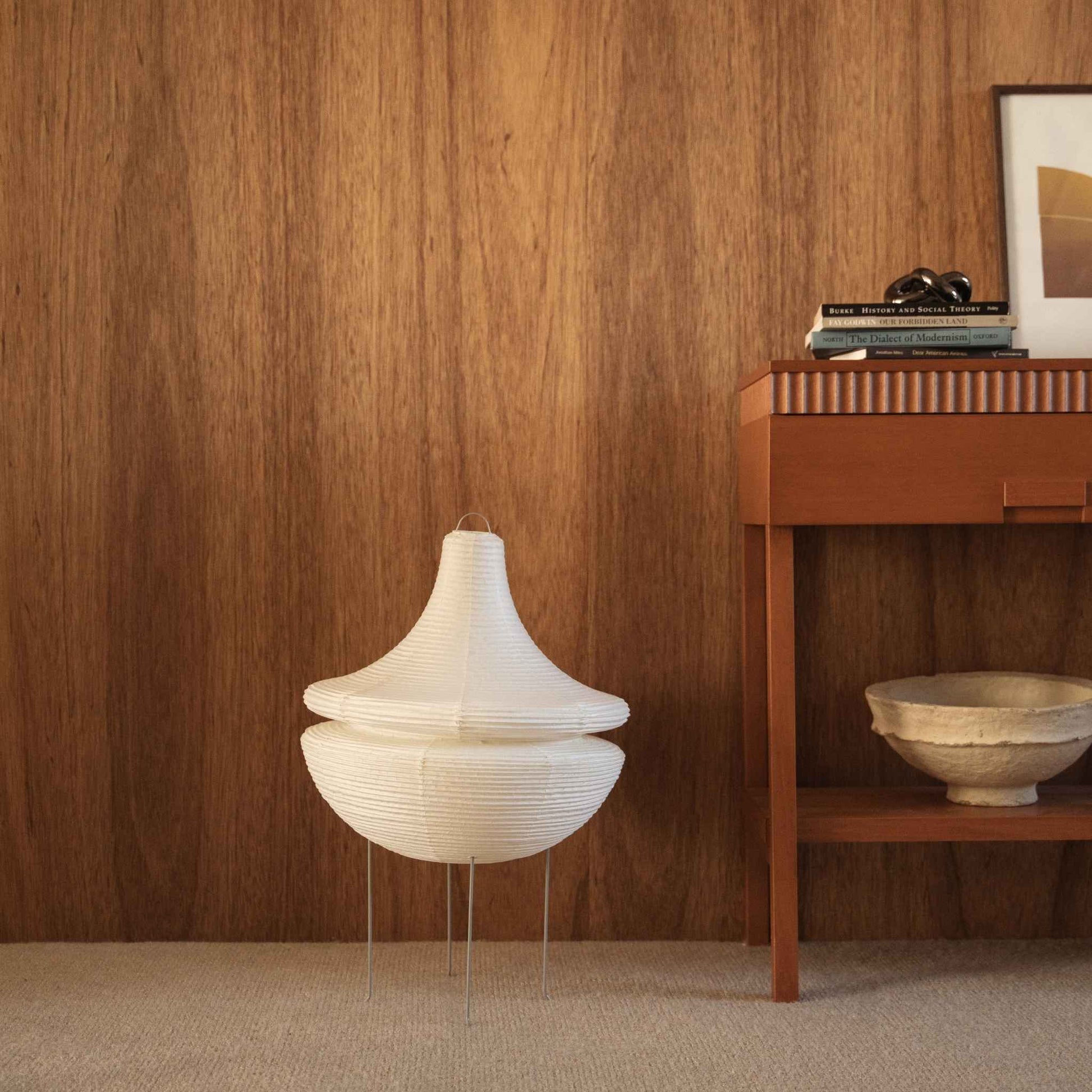 Unlit Japanese paper floor lamp Gemini 02 standing on a carpeted floor next to a wooden console table against a dark wall