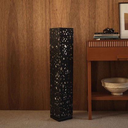 Black Me Look 01 paper floor lamp standing unlit on a carpet against a dark wood wall near a console table.