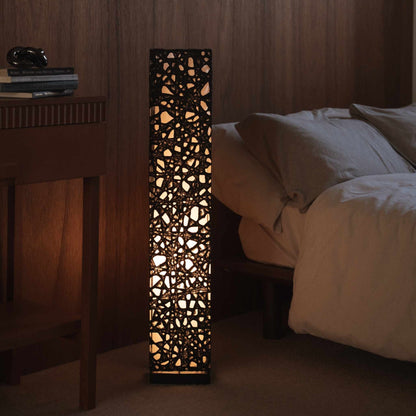 Lit black Japanese paper floor lamp Me Look 01 standing next to a bed in a dim japanese bedroom context.