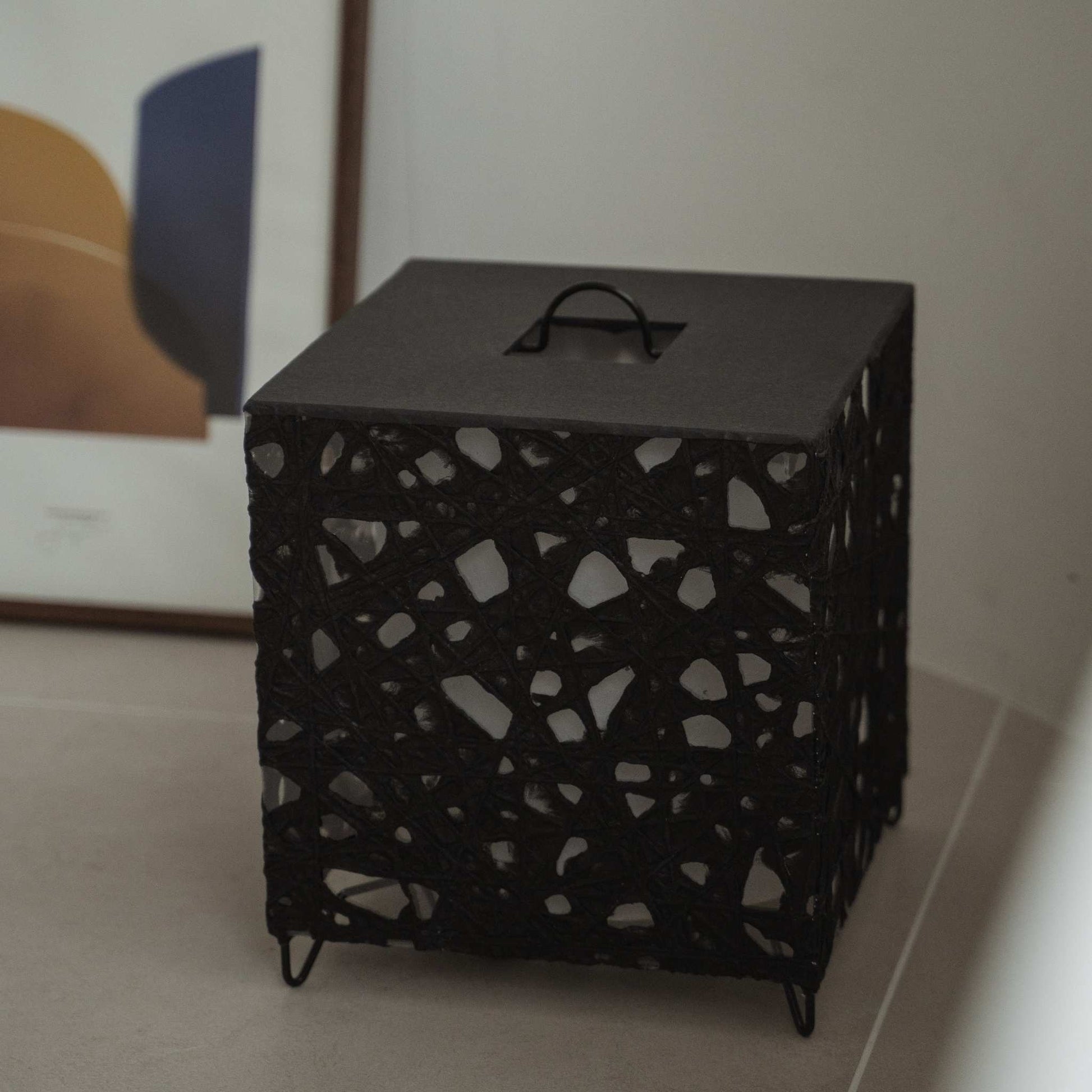 Unlit black cube Japanese floor lamp Me Look 03 sitting on a beige tiled floor next to a framed art print