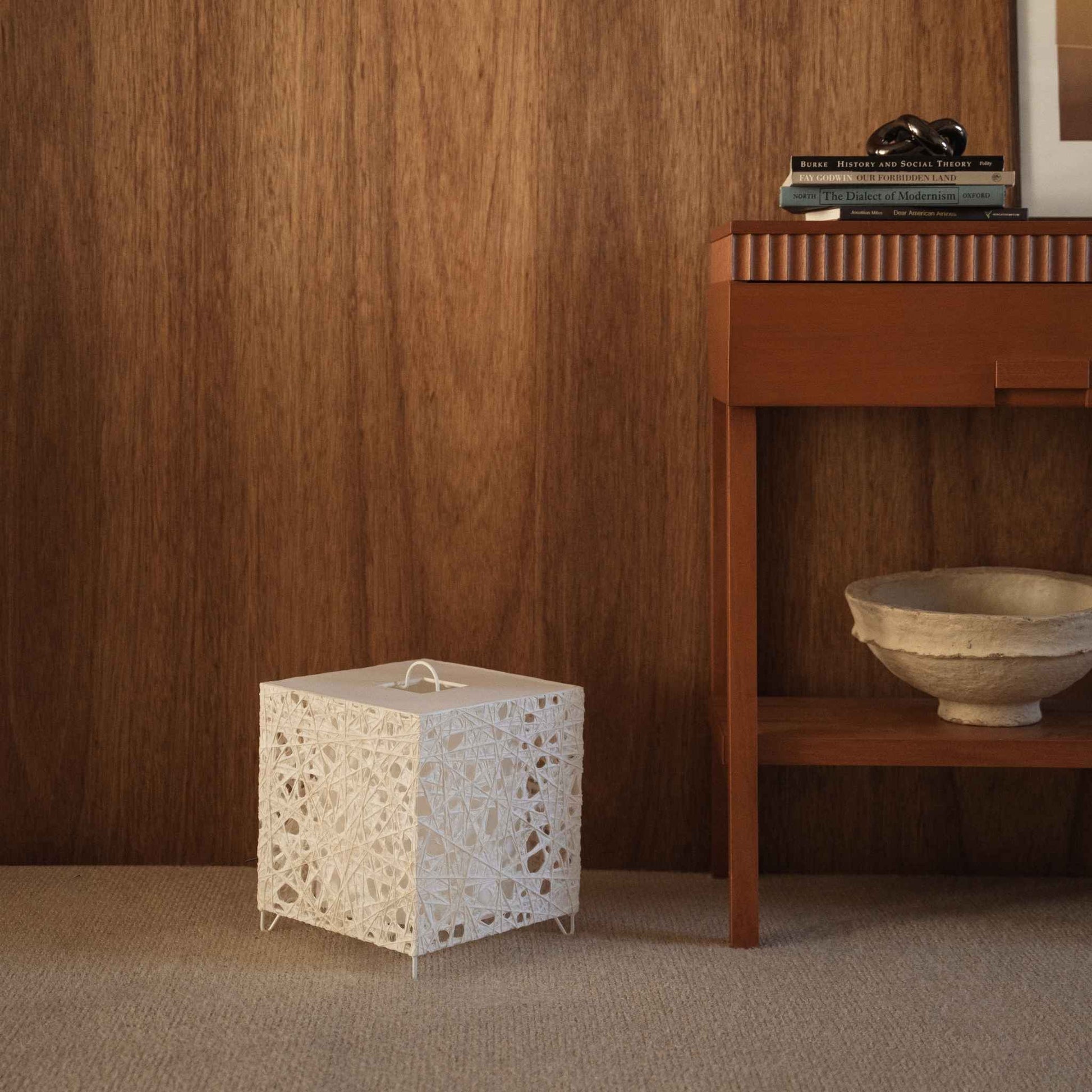 Cube shaped white paper floor lamp Me-Look 03 standing on a beige carpet against a dark wooden wall in a living room