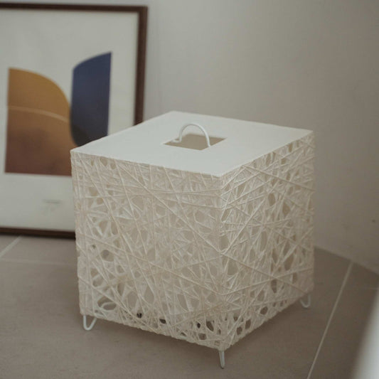 Unlit white cube Japanese floor lamp Me Look 03 sitting on a beige tiled floor next to a framed art print