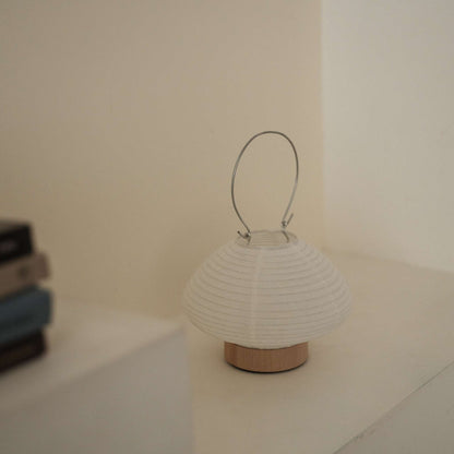 A portable japanese paper lamp RIN 01 with a metal handle sitting on a white surface showing its delicate mino washi texture