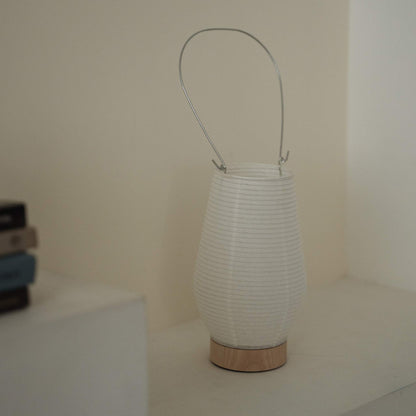 A portable japanese paper lamp RIN 02 with a metal handle sitting on a white surface showing its delicate mino washi texture