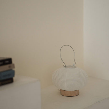 A portable japanese paper lamp RIN 03 with a metal handle sitting on a white surface showing its delicate mino washi texture