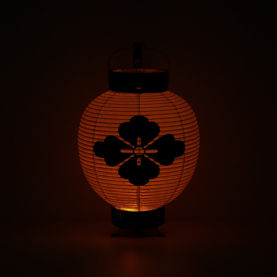A flower diamond Japanese lantern lit up in the dark casting a meditative orange light through the paper body.
