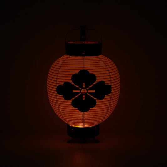 A flower diamond Japanese lantern lit up in the dark casting a meditative orange light through the paper body.