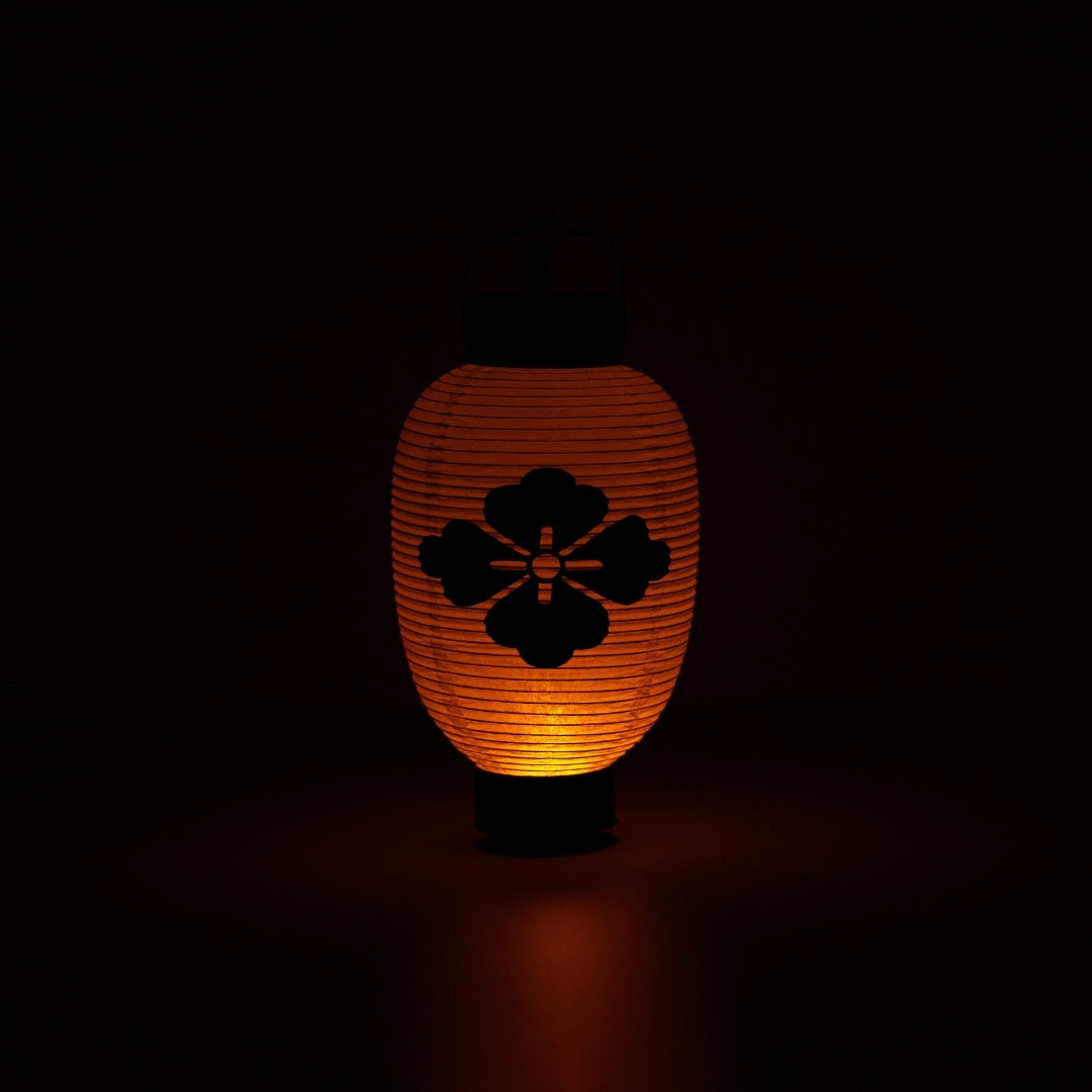 A glowing flower diamond japanese lantern illuminating a dark space with a soft and meditative orange light.