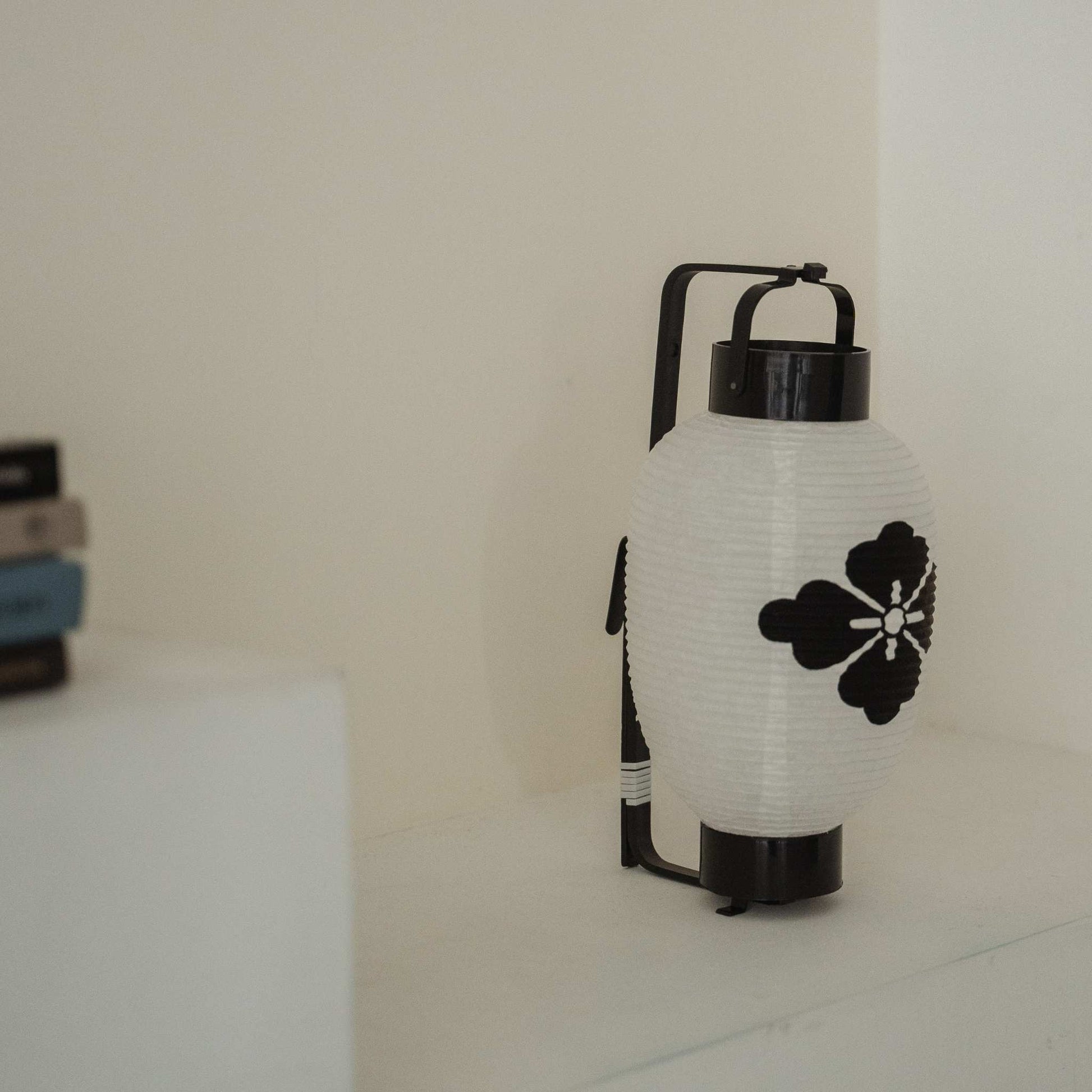 Side profile of a standing paper lantern showing the black bamboo bow structure against a white wall.