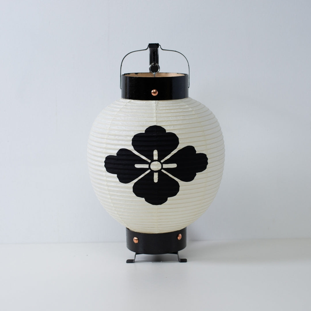 A small Japanese paper lantern featuring a hand-painted black flower diamond crest on white washi paper.