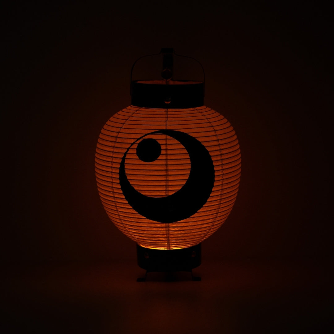A Japanese paper lantern illuminating a warm orange glow in a dark room highlighting the moon and star ink painting.