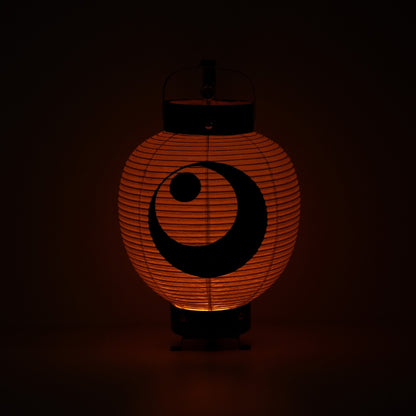 A Japanese paper lantern illuminating a warm orange glow in a dark room highlighting the moon and star ink painting.