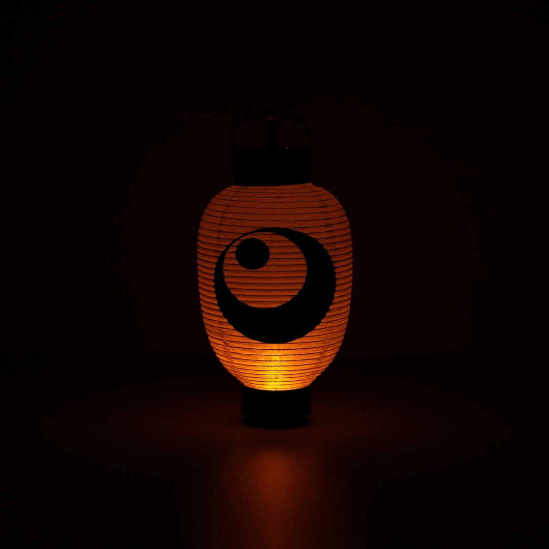 Illuminated Japanese paper lantern with a moon and star design casting a warm orange glow in a dark room.