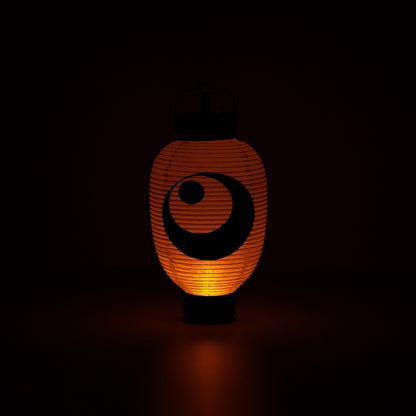 Illuminated Japanese paper lantern with a moon and star design casting a warm orange glow in a dark room.