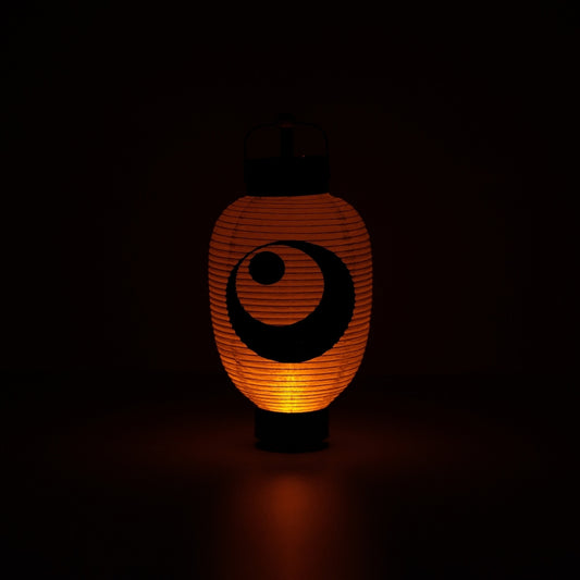 Illuminated Japanese paper lantern with a moon and star design casting a warm orange glow in a dark room.