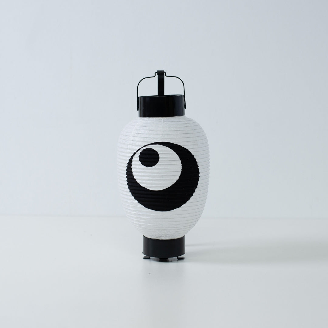 A white Japanese paper lantern with a hand-painted black moon and star motif standing on a white surface.