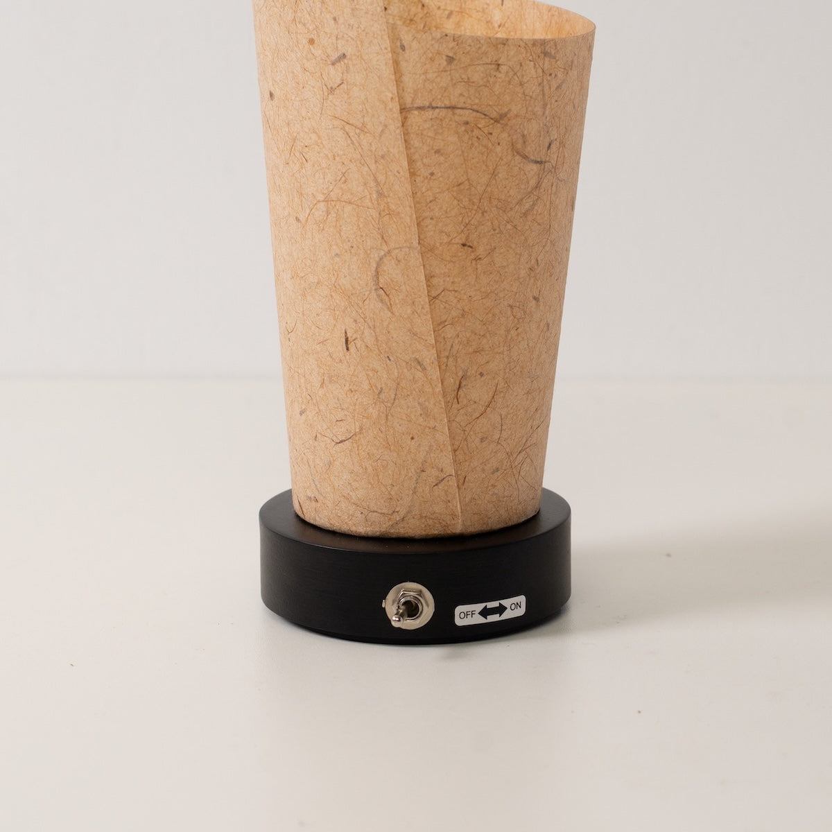 Japanese Paper Table Lamp "Maki" Cedar Bark, brown, wood - close-up of the black base and toggle switch for the cordless lamp.