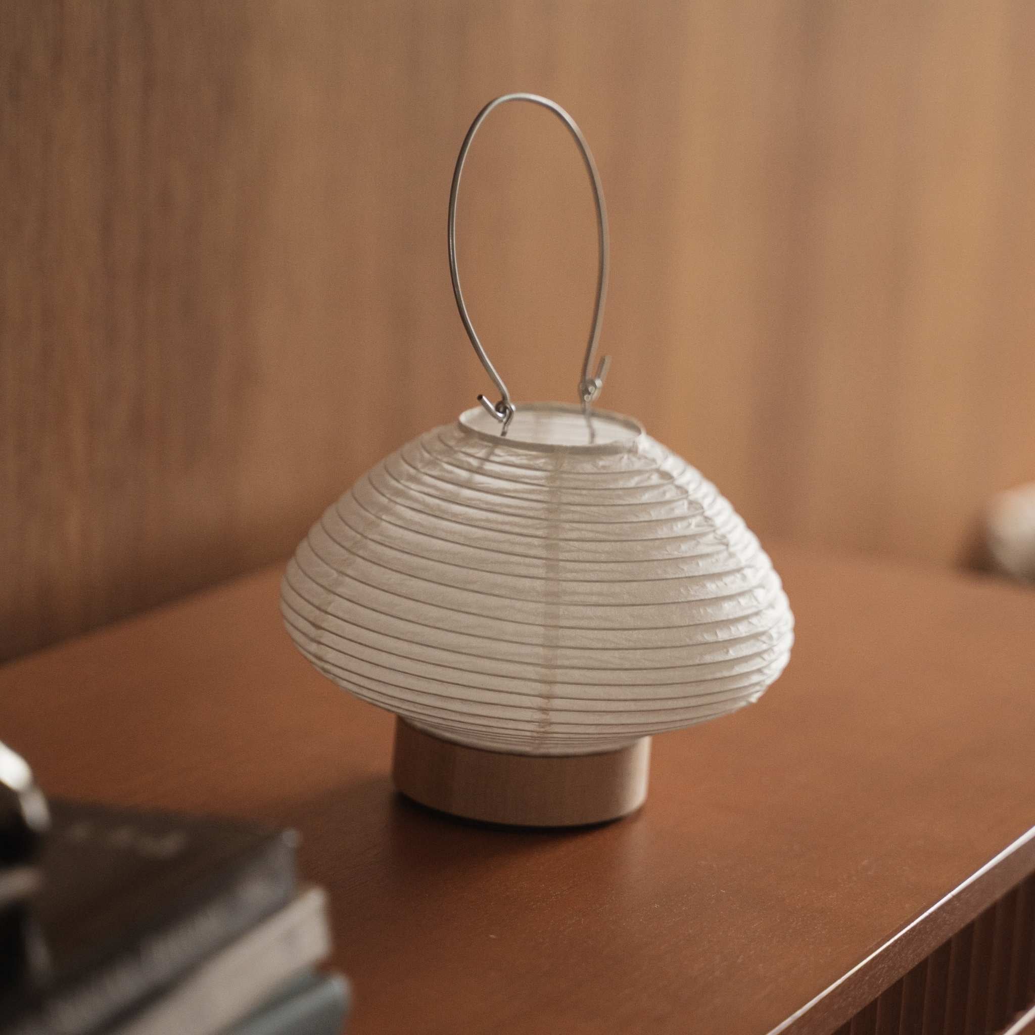 Small japanese paper table lamp Rin 01 sitting on a brown wooden console table showcasing its round white shape