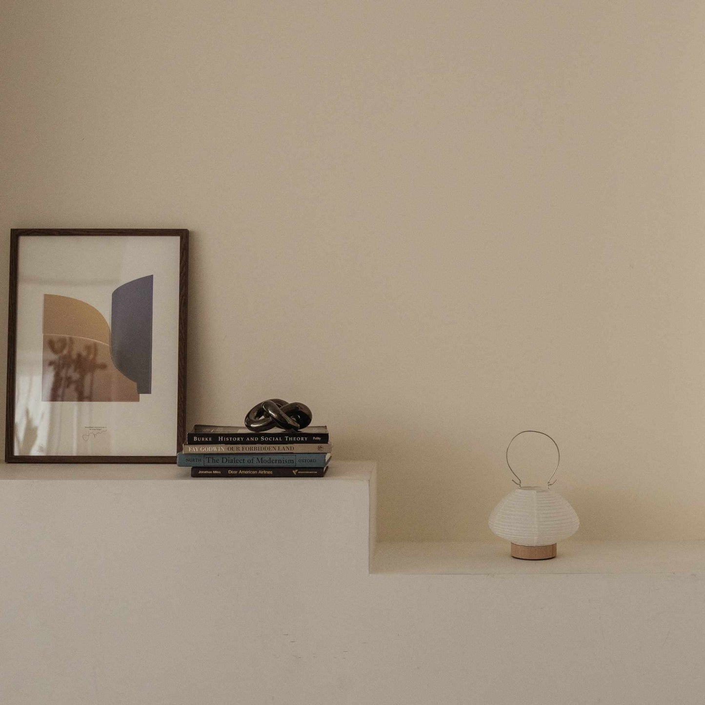 Unlit japanese paper table lamp RIN 01 placed on a white shelf next to books and art in a japandi style room