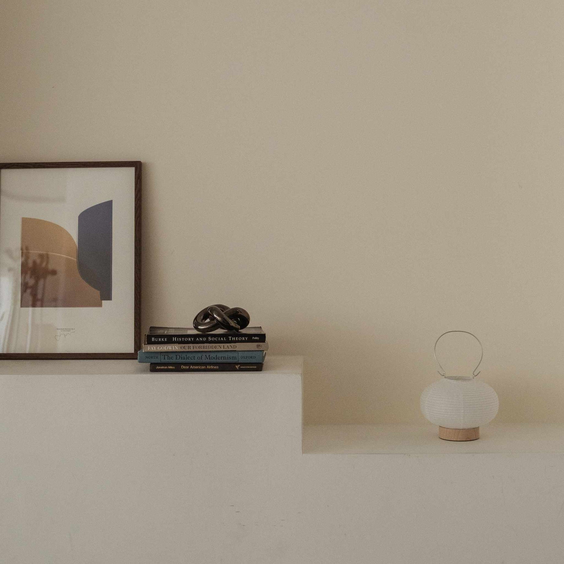 Unlit japanese paper table lamp RIN 03 placed on a white shelf next to books and art in a japandi style room