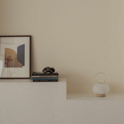 Unlit japanese paper table lamp RIN 03 placed on a white shelf next to books and art in a japandi style room