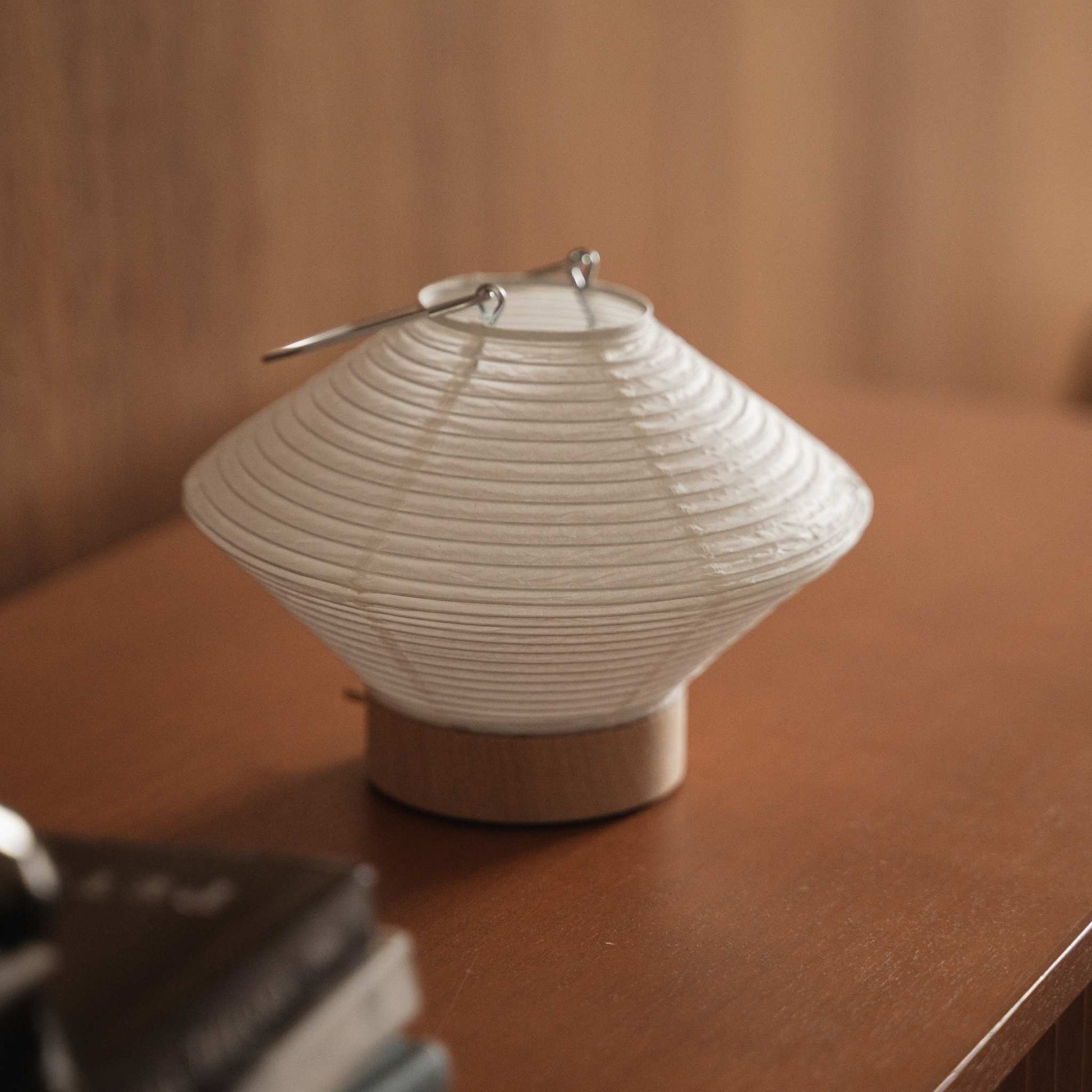 Small japanese paper table lamp Rin 05 sitting on a brown wooden console table showcasing its round white shape
