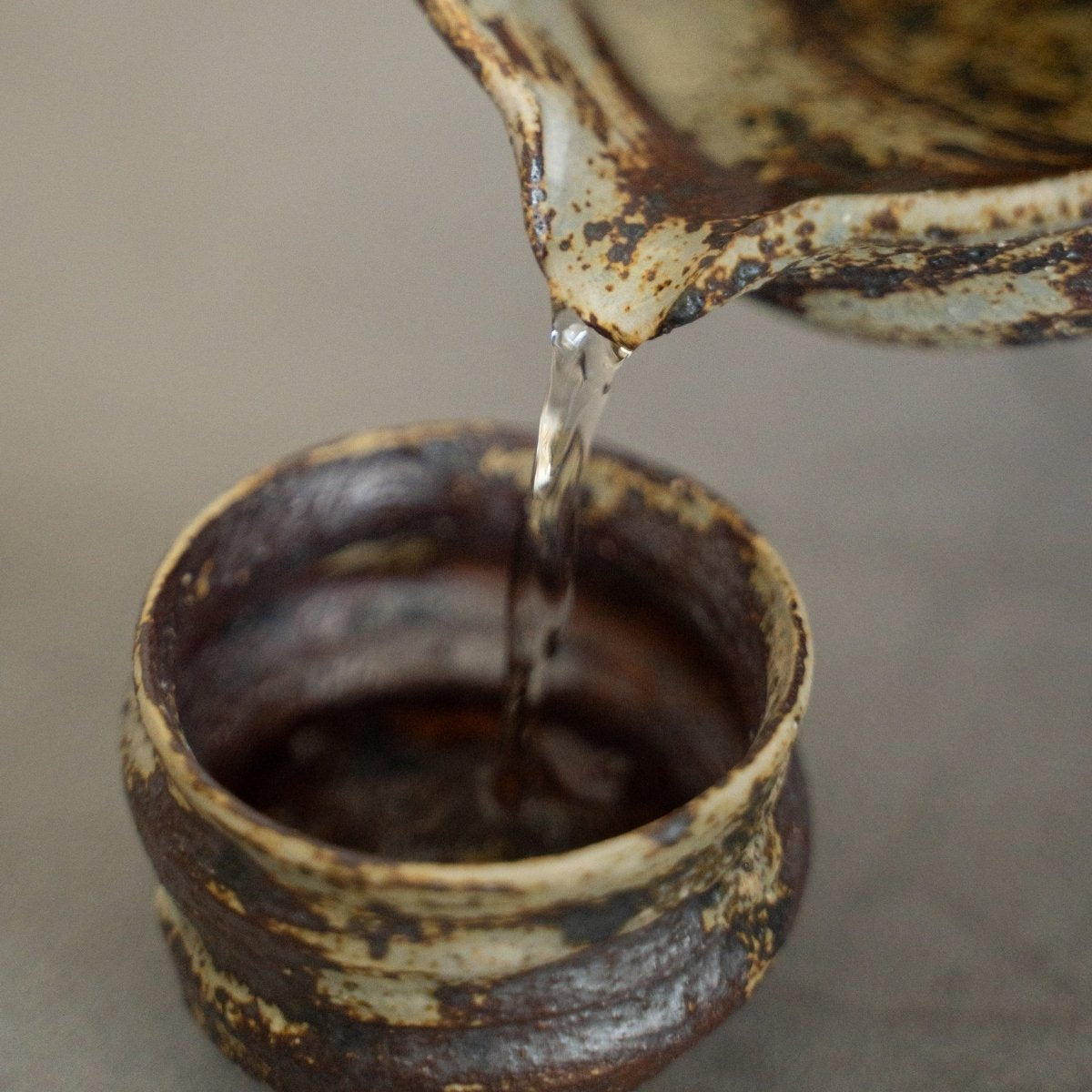 Rustikale japanische Sake-Karaffe, die Sake in eine Tasse gießt, damit eine Person ein reichhaltiges und aromatisches Getränk genießen kann.