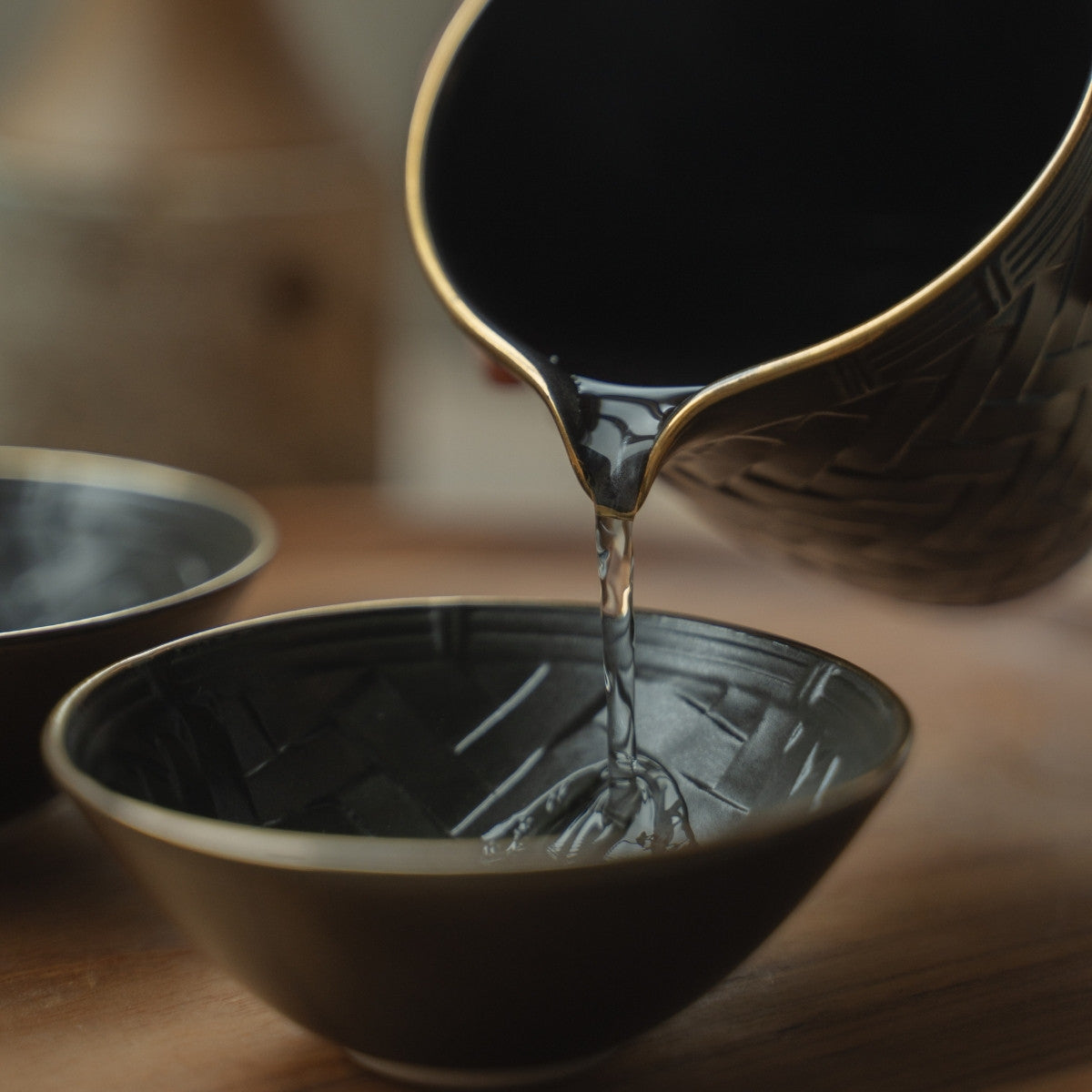 Serving clear liquid from a dark sake carafe into a black basket weave sake cup, perfect for elegant gatherings.