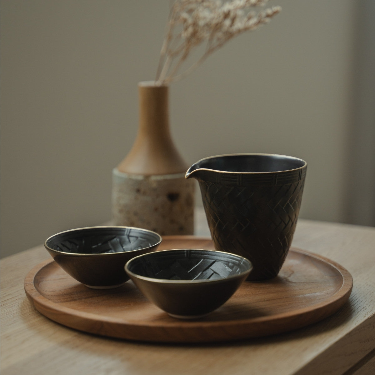 Black arita porcelain sake carafe and sake cups on a wooden tray, set for a mindful modern dining experience.