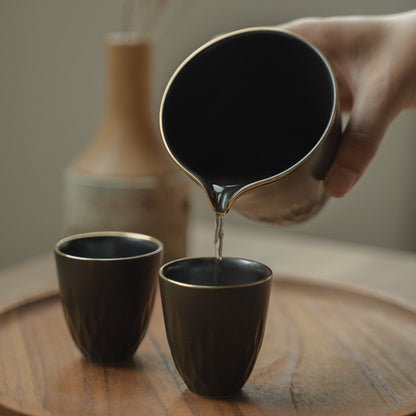 Hand pouring from a matte black Japanese sake pitcher into a matching cup on a tray, elevating a special dinner gathering.