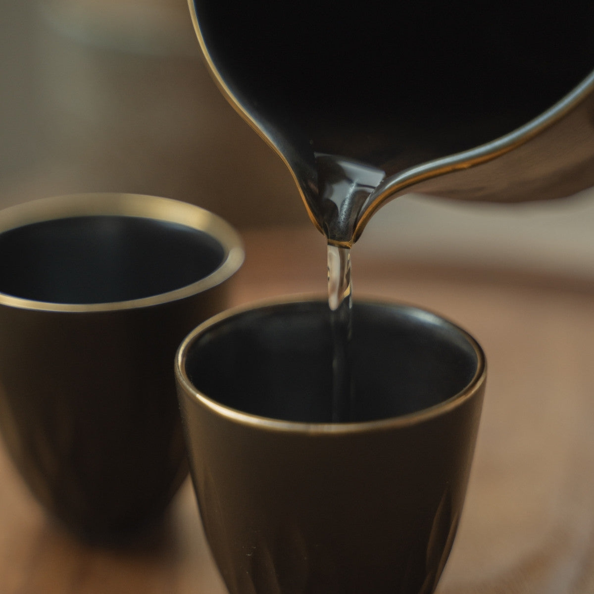 Close-up of pouring clear sake from a black sake carafe into a gold-rimmed sake cup, enhancing a luxurious dining moment.