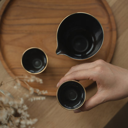 Hand holding a black sake cup showing its silver interior over a wooden tray, preparing for a mindful evening sake ritual.