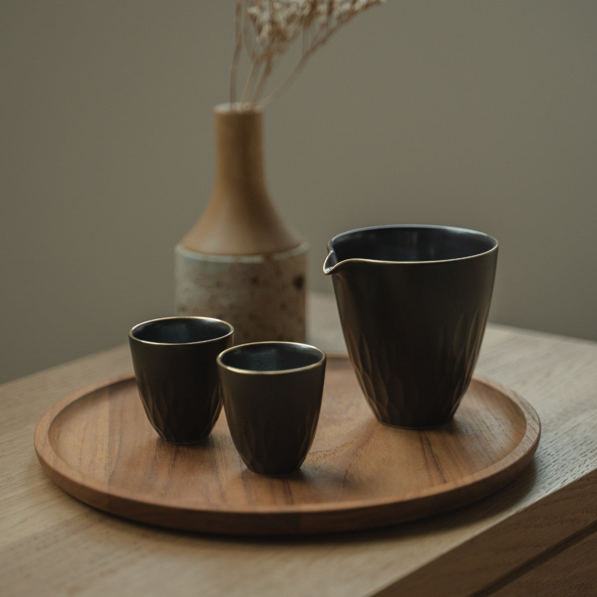 Dark arita porcelain sake pitcher and guinomi cups on a wooden tray, inviting sake lovers to a refined evening gathering.