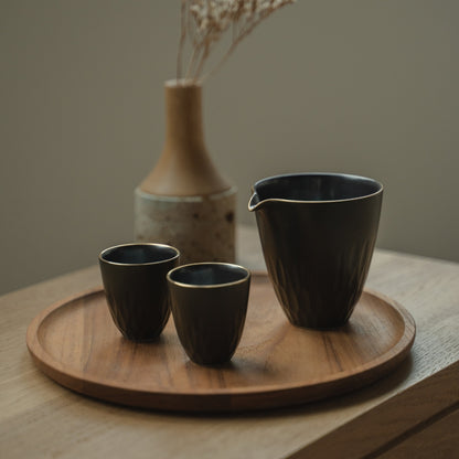 Dark arita porcelain sake pitcher and guinomi cups on a wooden tray, inviting sake lovers to a refined evening gathering.
