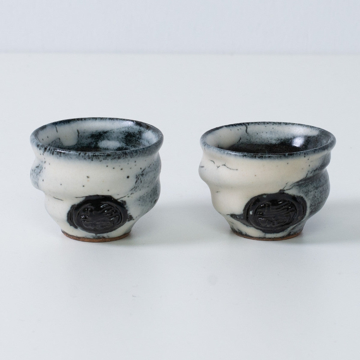 Zwei weiße und schwarze japanische Sake-Becher Ochoko aus Keramik von Creative Cloud aus Japan, mit eingraviertem schwarzem Künstlerstempel auf der Vorderseite.