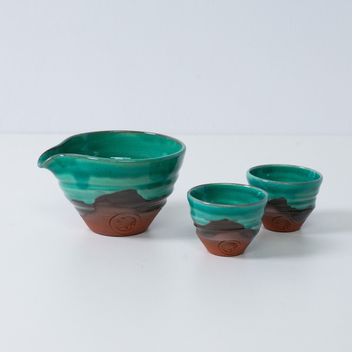 Sake-Set "Emerald" aus Keramik in Smaragdgrün und Orange, bestehend aus einer Katakuchi-Sake-Karaffe und zwei kleinen Bechern aus rotem Ton.